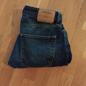Mörkblå jeans från Jack & Jones - Säljer ett par klassiska mörkblå jeans från Jack & Jones med raka ben och normal passform. Byxorna har fem fickor och en snygg läderpatch med logga bak i midjan. Perfekta till vardags och enkla att matcha med olika stilar.