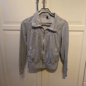 Grå zip-hoodie med krage - Grå hoodie med dragkedja framtill och hög krage. Tillverkad i mjukt material med ribbade muddar vid ärmslut och nederkant. I strl 40