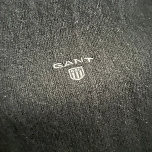 Svart ziptröja från GANT - Säljer en svart ziptröja från GANT i mjukt material. Tröjan har hel dragkedja framtill, ståkrage med grå insida och diskret GANT-logga på bröstet. Perfekt för lager-på-lager och enkel att matcha med det mesta.