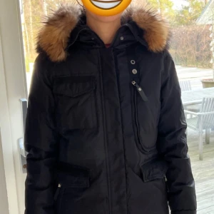 Hollies jacka  - Säljer en svart jacka från Hollies med äkta päls. Draget på en dragkedja är utbytt då original gick sönder. Jackan är liten i storleken. Modellen är 175cm.