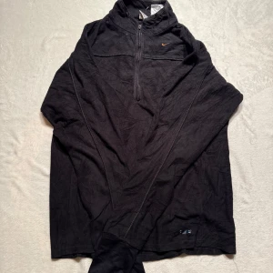 Retro fleece half zip Nike - Svart retro fleece tröja från Nike half zip. klassiska Nike-loggan i orange på bröstet. Lite tunnare material, perfekt för våren.