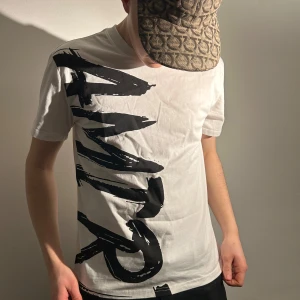 Vit t-shirt med tryck amiri  - Snygg vit t-shirt med stort svart tryck på framsidan. Perfekt för en avslappnad stil. Kortärmad och i en skön passform.