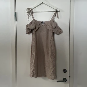 Beige klänning från H&M  - Säljer en söt beige klänning från H&M med puffiga ärmar och knytband vid axlarna. Perfekt för en somrig look! 💫 Aldrig använd prislappen finns kvar
