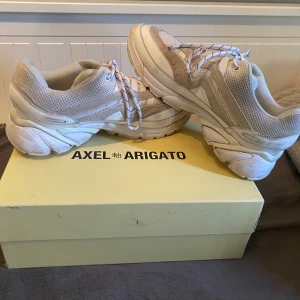 Vita sneakers från Axel Arigato - Säljer ett par stilrena vita sneakers från Axel Arigato. Skorna har en chunky sula och är tillverkade i en kombination av syntetmaterial och mesh för en modern look. Perfekta för en casual stil. En tvätt och skicket är 9/10, box och dustbag medföljer självklart!