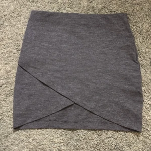 Grå kjol från Gina Tricot - Snygg grå kjol från Gina Tricot i omlott-design. Köpt secondhand, knappt använd! Perfekt för en stilren look. Kjolen är kort och har en enkel men elegant stil❣️