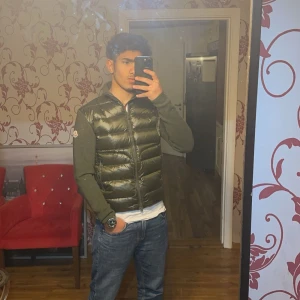 Grön Moncler cardigan - Snygg grön pufferjacka från Moncler med dragkedja framtill. Jackan har långa ärmar och en glansig finish som ger en modern look. Perfekt för kyligare dagar när du vill hålla stilen. 🧥