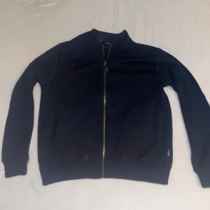 Svart långärmad tröja med dragkedja - Säljer en stilren svart långärmad tröja med dragkedja framtill. Perfekt för en avslappnad look. Tröjan har en enkel design och är lätt att matcha med andra plagg.