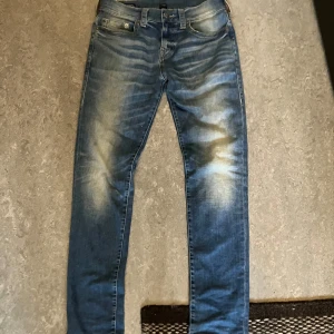 Blå jeans från True Religion - Snygga blå jeans från True Religion med en klassisk femficksdesign och märkets ikoniska logga på bakfickan. Jeansen har en lätt tvättad look och är perfekta för en avslappnad stil. De har en knappgylf och bälteshällor. 