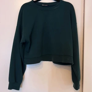 Mörkgrön sweatshirt från Zara - Säljer en mörkgrön sweatshirt från Zara. Tröjan har en croppad design med långa ärmar och ribbade muddar vid ärmslut och nederkant. Det är storlek S