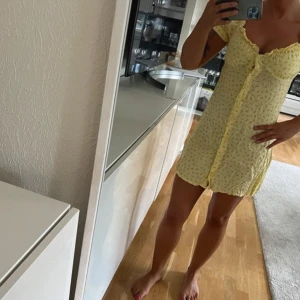 Gul blommig klänning - Söt gul klänning med små blommor och knappar framtill. Den har korta ärmar och en luftig passform, perfekt för varma dagar. Klänningen är gjord i ett lätt material som ger en skön känsla. Använd en gång 