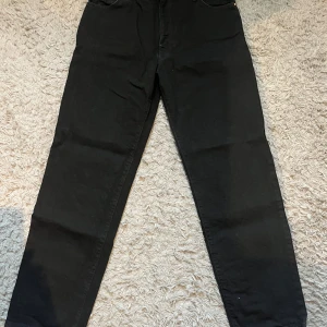 Svarta jeans från Woodbird - Snygga svarta jeans från Woodbird i en klassisk design. De har en rak passform och är perfekta för en stilren look. Jeansen har fem fickor och en knappgylf.