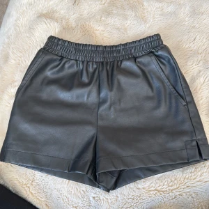 Svarta shorts från Designers Remix - Snygga svarta skinnshorts från Designers Remix i syntetmaterial. De har en elastisk midja för extra komfort. Dom här skinnshortsen är från Lucca 