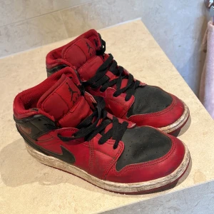 Röda och svarta Nike Air sneakers - Snygga röda och svarta Nike Air sneakers med klassisk design. Skorna har svarta snören och en vit sula med röd undersida. Perfekta för en sportig look.