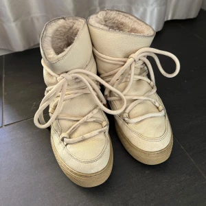 Beige vinterboots från Inuikii - Säljer ett par snygga beige vinterboots från Inuikii. De är fodrade med päls för extra värme och har snörning framtill. Perfekta för kalla dagar med stil.