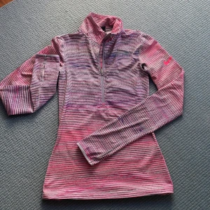 Randig träningströja från Nike - Säljer en randig träningströja från Nike i Dri-Fit material. Tröjan har en dragkedja framtill och är i färgerna rosa, blå och vit. Perfekt för träning med sin långärmade design och bekväma passform.