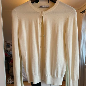 Beige kofta från Zara - Säljer en stilren beige kofta från Zara med rund halsringning och knappar framtill. Perfekt för lager-på-lager och passar till många olika outfits. Ett måste i garderoben för en klassisk look.