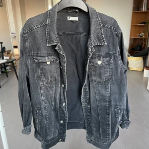 Grå jeansjacka  - Snygg grå jeansjacka med klassisk krage och knappar framtill. Jackan har två bröstfickor med lock och knappar samt långa ärmar med knappslut. Perfekt för en casual look!