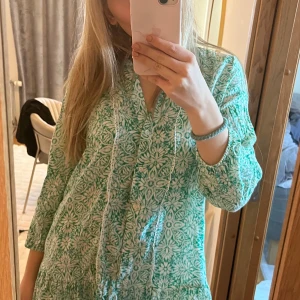 Grön och vit blommig klänning - Säljer en söt grön och vit klänning med blommigt mönster. Klänningen har trekvartsärmar och en v-ringad design med fina spetsdetaljer. Perfekt för en somrig look! 🌸