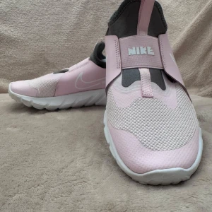 Rosa och grå Nike sneakers - Säljer ett par stilrena Nike sneakers i rosa och grått. Skorna har en unik design med elastiska band och en vit sula. Perfekta för en sportig look.