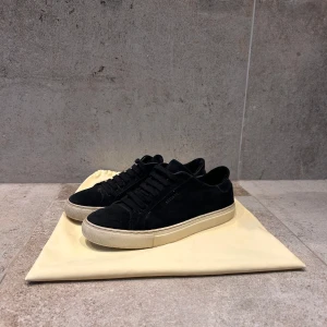 Svarta sneakers från Axel Arigato - Snygga svarta sneakers i mocka från Axel Arigato med vit sula. I storlek 38. Skorna har en stilren design med snörning och subtil branding på sidan. Perfekta för en avslappnad och trendig look. Några mindre defekter finns, skicka privat för att se bilderna. Nypris 2499kr                                                                             Hör av dig vid möjliga frågor 