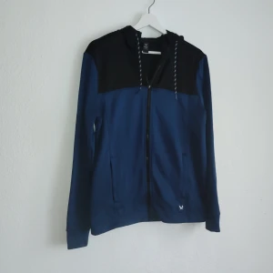 Blå och svart jacka från SOC - Säljer en snygg blå och svart jacka från SOC med dragkedja och huva. Jackan har långa ärmar och en stilren design med en liten logga på framsidan. Perfekt för en casual look.