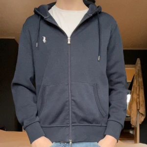 Mörkblå hoodie från Ralph Lauren - Säljer en snygg mörkblå hoodie från Ralph Lauren med dragkedja och det klassiska logotypbroderiet på bröstet. Pris är diskuterbart och skicket är 10/10! Nästan som ny! Hör av er vid minsta fråga😁