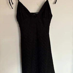 Svart klänning med spetsdetaljer - Snygg svart klänning med spetsdetaljer och smala axelband med knyt detaljer. Perfekt inför sommaren. Klänningen har en v-ringad design. 