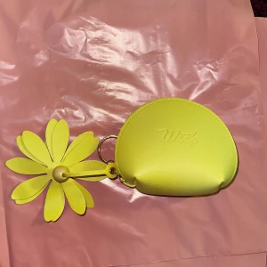 Plånbok med blomdetalj - Gul plånbok med en stor blomdetalj. Plånboken har en dragkedja och är perfekt för att hålla småsaker. Den är kompakt och lätt att bära med sig.