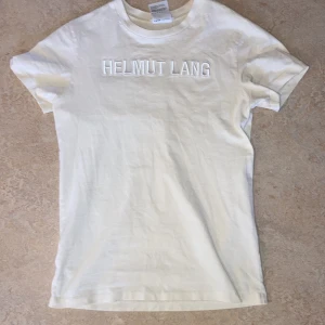 Vit Helmut Lang t shirt - Säljer nu en till av mina Helmut Lang t-shirts. Är väl unisex S för män o M för kvinnor. Modellen är 178,65kg. Den texturerade loggan är en fin design. Den är lite off white och rätt skönt material
