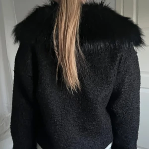 Svart jacka med pälsdetalj - Snygg svart jacka från Chelsea med en fluffig pälsdetalj vid kragen. Jackan har knappar framtill samt två fickor på bröstet. Perfekt för att ge en stilren look. Använd fåtal gånger köpt för 799kr. 😊🥰