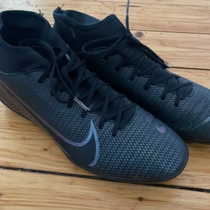 Svarta fotbollsskor från Nike - Snygga svarta fotbollsskor från Nike med snörning och en stilren design. Skorna har en diskret Nike-logga på sidan och är perfekta för fotbollsplanen. De har en tight passform och är gjorda i syntetmaterial för bästa prestanda. Ett par svarta benskydd från soc ingår även i priset. Allt ser väldigt nytt ut och har nästan knappt används. Priset kan diskuteras :) 