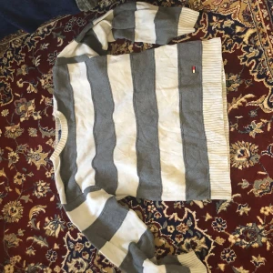 Randig tröja från Tommy Hilfiger - Säljer en snygg randig tröja från Tommy Hilfiger i grått och vitt. Tröjan är tillverkad i bomull och har långa ärmar med ribbade muddar. Lite fläckar se bild