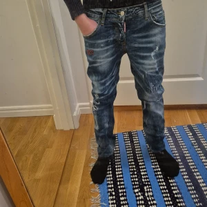 Blå jeans från Dsquared2 - Snygga blå jeans från Dsquared2 med slitna detaljer och broderad logga. De har en klassisk femficksdesign och knappgylf. Perfekta för en avslappnad stil med en touch av edge.står att de är w31 men de sitter hundra procent som en W28 L32