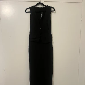 Svart långklänning från Boohoo - Elegant svart kostym långklänning från Boohoo med djup v-ringning och ärmlös design. Perfekt för en stilren look. 