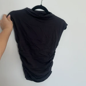 Svart topp från Gina Tricot - Säljer en stilren svart topp från Gina Tricot i storlek XS. Toppen har en enkel design med korta ärmar och är tillverkad i ett mjukt material som ger en bekväm passform.