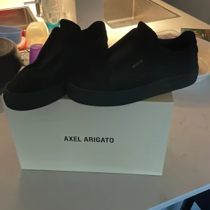 Svarta sneakers från Axel Arigato storlek 42  - Snygga svarta sneakers från Axel Arigato. Stilren design med diskret logga på sidan. Köpta på Arigato butiken i Stockholm. Använda ett fåtal gånger och ser ut som nya. Skopåse och original box kommer med!