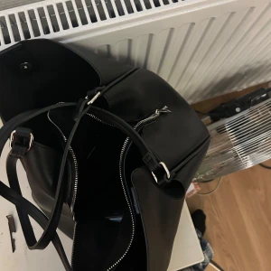 Svart axelväska med dragkedja - Snygg svart axelväska med dragkedja. Väskan har en minimalistisk design och är lätt att matcha med olika outfits. Väskan e som ny. Från Vera Moda.