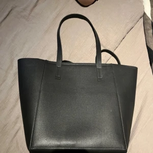 Svart toteväska UNIQLO - Snygg och stilren svart axelväska i skinn. Använd få gånger och är perfekt när man ska iväg eller använda i sin vardag. Rymlig och har inga anmärkningar 