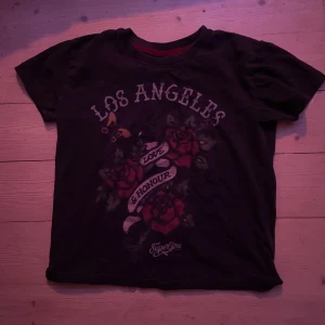 Svart t-shirt med tryck från Superdry - Cool svart t-shirt från Superdry med tryck av rosor och texten 'Los Angeles Love & Honour'. Perfekt för en avslappnad stil med en touch av attityd.