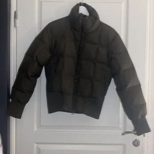 Olivgrön pufferjacka från Boomerang - Snygg olivgrön pufferjacka från Boomerang i storlek S. Jackan har en quiltad design med dragkedja och ribbade muddar vid ärmslut och nederkant. Perfekt för kyligare dagar med sin varma och stilrena look.