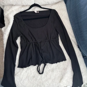 Svart topp med knytband - Snygg svart topp med långa ärmar och knytband i midjan. Perfekt för en stilren look. Verkligen så fiiin!!! Har inte använt någon gång så säljer därav💕🌸💕🌸🌸