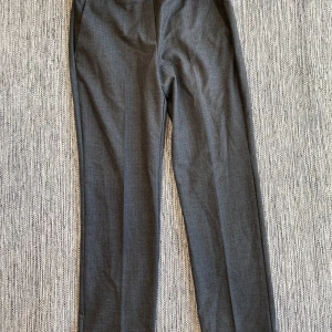 Grå kostymbyxor från MAX&Co. - Snygga grå kostymbyxor från MAX&Co. med ett subtilt fiskbensmönster. Byxorna har en klassisk rak passform och är perfekta för en stilren look. Tillverkade i ett bekvämt material som ger en elegant känsla. Nya grå mönstrade kostymbyxor i strl 40 från MAX&Co.  Nya, aldrig använda.  Mått Midjan: ca 41 cm Längd från grenen och ner: ca 74 cm  64% polyester, 12% viskos och 4% elastan  Kommer från ett djur och rökfritt hem. 