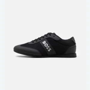 Svarta sneakers från BOSS - Helt oanvända stilrena svarta sneakers från BOSS med snörning och logotyp på sidan. Skorna har en modern design med en kombination av syntetmaterial och textil för en bekväm passform. 