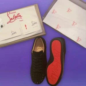 Svarta sneakers från Christian Louboutin - Snygga svarta sneakers från Christian Louboutin med ikoniska röda sulor. Skorna har en cool design med nitar på tån och är tillverkade i mocka. Perfekta för att ge din stil en edgy touch.