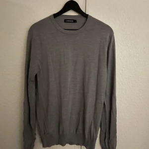 Grå tröja från J.Lindeberg - Säljer en stilren grå tröja från J.Lindeberg. Tröjan har en klassisk rund hals och långa ärmar. Perfekt för en avslappnad och snygg look. Använd fåtal gånger