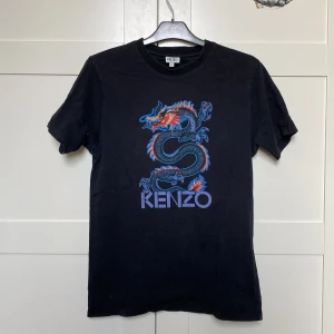 Kenzo T-shirt - Svart Kenzo tshirt säljes nu i bra skick. Köptes för 1300kr och är sällsynst idag. Säljer denna nu då jag är i behov av pengar! Perfekt för att ge din outfit en unik touch. T-shirten är kortärmad och gjord i mjuk bomull för extra komfort. Storlek: Small