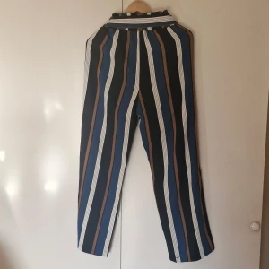 Randiga byxor med knytband - Snygga randiga byxor i blått, brunt och vitt med hög midja och knytband. Perfekta för en stilren look med en loose passform.