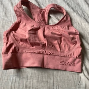 Rosa sporttopp från Exani - Säljer en rosa sporttopp från Exani i storlek M. Tillverkad av 95% polyamid och 5% elastan för en bekväm och stretchig passform. Perfekt för träning med sin tighta passning och stilrena design.