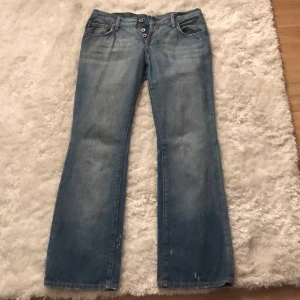 Blå ralph lauren bootcut jeans - Snygga blå bootcut jeans med knappar framtill. De har en klassisk femficksdesign och en lätt tvättad look. Perfekta för en avslappnad stil. Mått står på bilden längst bak