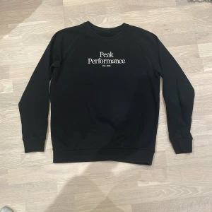 Svart tröja från Peak Performance - Säljer en stilren svart tröja från Peak Performance med vit text på bröstet. Tröjan har långa ärmar och en rund halsringning. Perfekt för en avslappnad stil. Använd väl men också väl omhändertagen. 